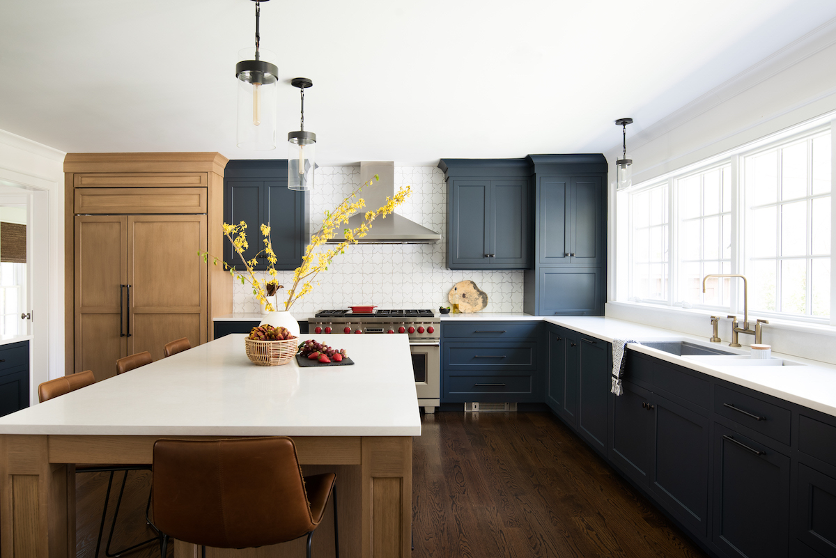 In this renovated Allendale home, the kitchen derives its warmth from the use of wood and navy on the cabinets, brightened by the white Caesarstone quartz countertops, the white Fireclay tile backsplash and a bank of large windows that open onto the backyard.