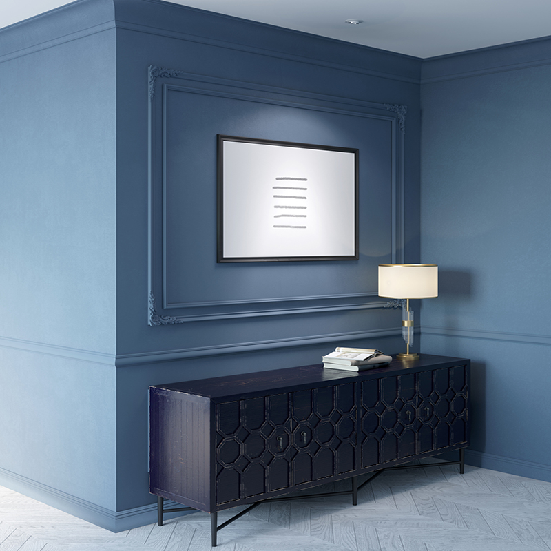 Classic interior in blue tones with an illuminated horizontal poster above an old black cabinet with a lamp and books on it, white parquet flooring, moldings on the walls.