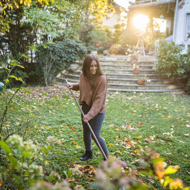 Happy woman sweeping garden with broom in back yard