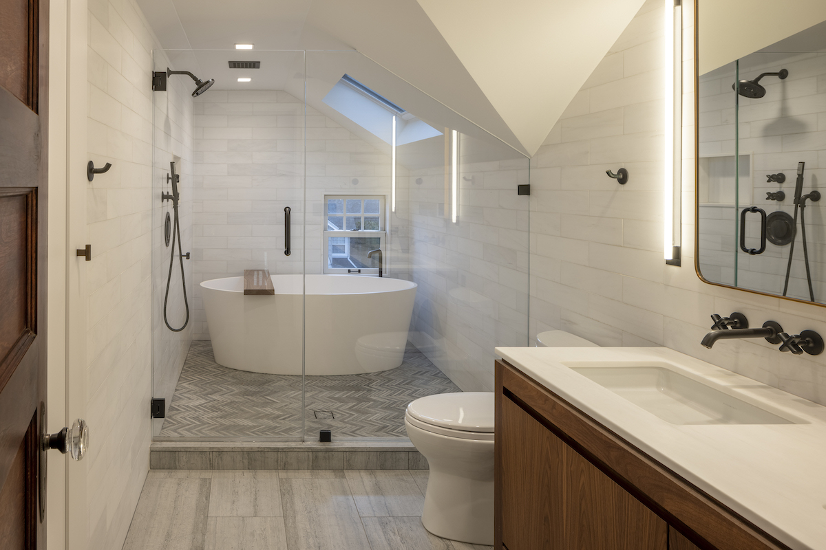 Originally dark and cramped, the primary bathroom was doubled in size and significantly brightened thanks to the installation of a skylight and the use of pale materials, like the wall, shower and floor tile from Stone Source and the Bianco Dolomiti vanity sink and topper, all from Stone Source. 