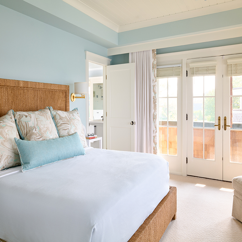 The master bedroom draws its serenity from water views and the coastal colors paired a woven lampakanai rope bed by Palecek.