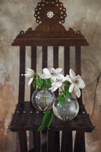 A large incense burner, tall candles in a tarnished silver candelabra and glass vases holding vines of clematis blossoms decorate a side table. There’s cozy seating too—stacks of Moroccan floor pillows, a silver leather pouf and a pair of metal chairs with a Moroccan wedding blanket.