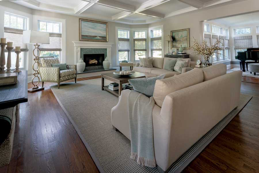 Designer Karyn Donohue blended Benjamin Moore Edgecomb Gray walls with the wood-tone furnishings to complete the family room and achieve an “elegantly casual” vibe. Furniture like the deep sofas, multi textured armchair and ottoman and coffee table echo the casual feel, while two serene prints, floor lamps and table accents add classic style.