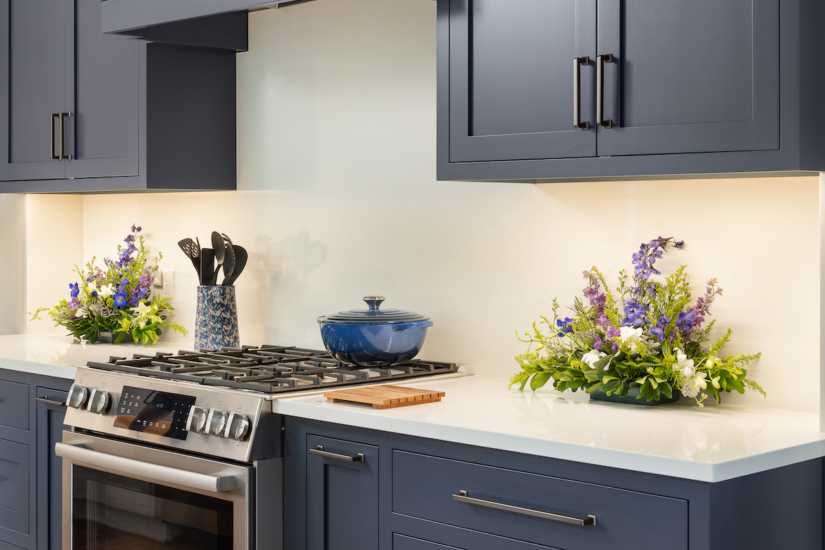 Indigo cabinets contrast the bright, high-gloss Smithfield Cambria quartz countertops and Benjamin Moore’s Wind’s Breath on the walls. Floors are pegged 5-inch red oak boards finished to match the window trim. 