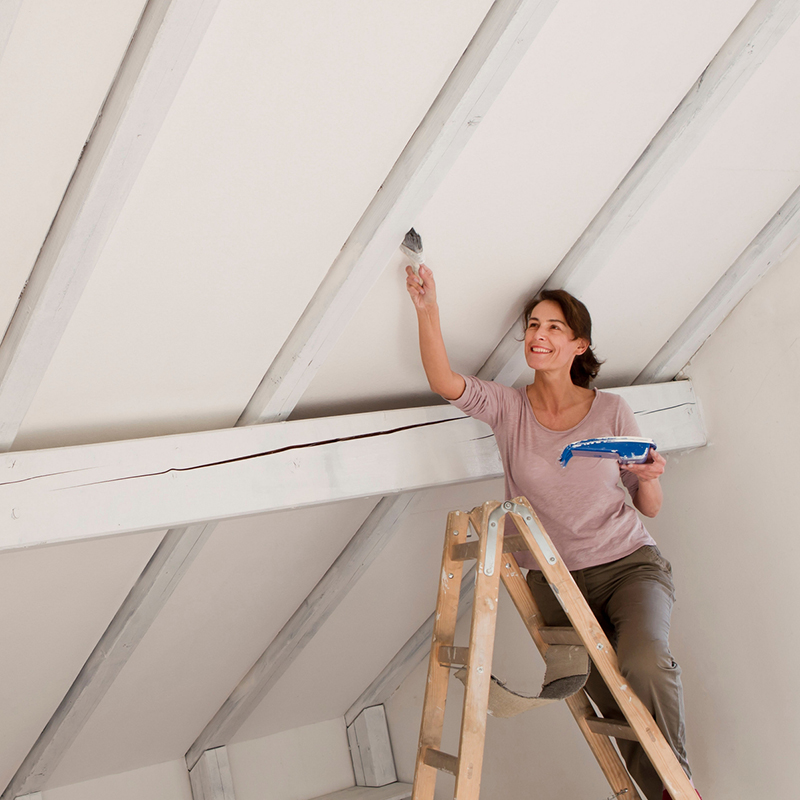 Woman on stepladders painting white ceiling